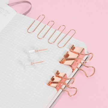 Rose gold paper clips, binder clips, and push pins on notebook
