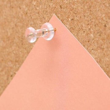 Clear push pin holding pink paper on standing cork board