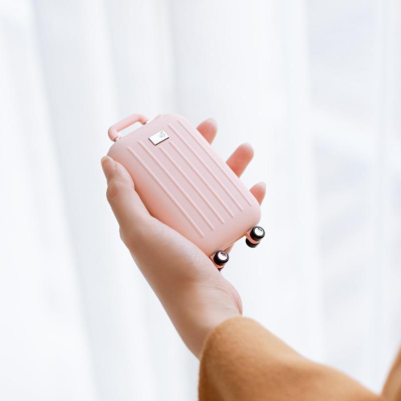 Traveler power bank in pink with hand warmer, shaped like a suitcase, in woman's hands